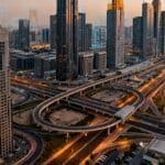 Aerial view of a modern city with tall skyscrapers, intersecting highways, and minimal traffic at sunset.