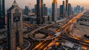 Aerial view of a modern city with tall skyscrapers, intersecting highways, and minimal traffic at sunset.