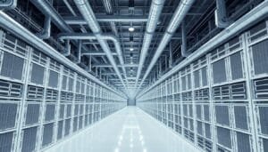 A hallway in a modern data center with rows of server racks on both sides and exposed ventilation pipes on the ceiling.