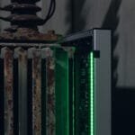 A close-up of an old, rusty radiator next to a modern device with green indicator lights in a dimly lit room.