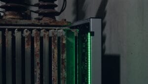 A close-up of an old, rusty radiator next to a modern device with green indicator lights in a dimly lit room.