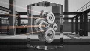 A group of interlocking gears encased in a transparent rectangular box, with beams of light passing through, set in an industrial environment.
