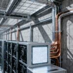 Rows of computer servers and cooling fans, supporting cutting-edge Neuro-Symbolic AI, are arranged along a corridor in an industrial room with exposed concrete walls and metal pipes.